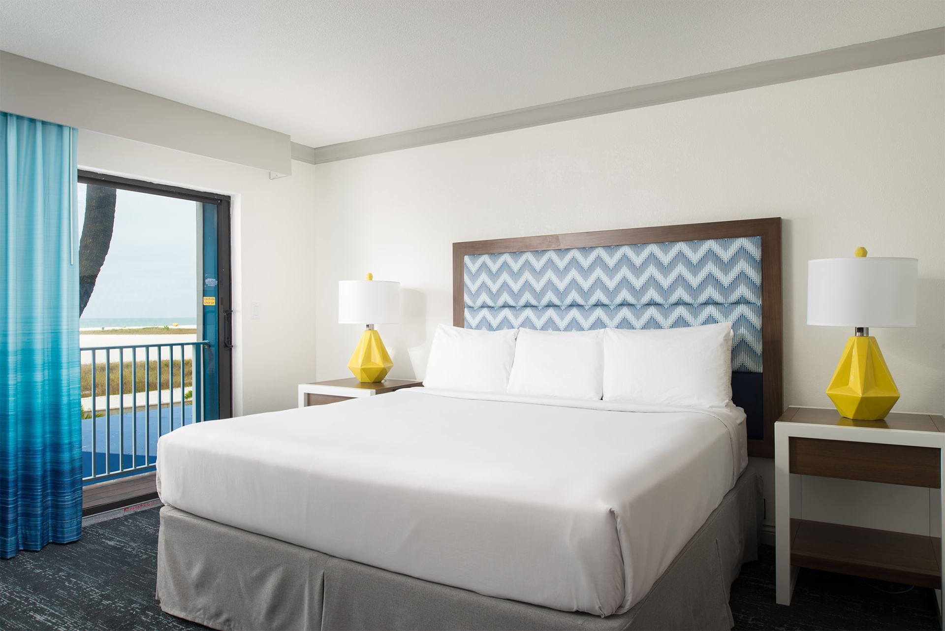 A hotel room with a king-sized bed, two nightstands with yellow lamps, and a balcony door.