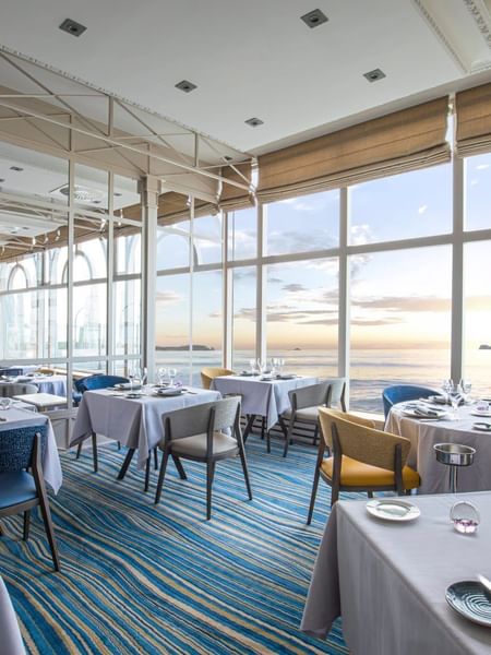 Le Cap Horn restaurant featuring dining tables & chairs overlooking the ocean at sunset at Le Grand Hôtel des Thermes