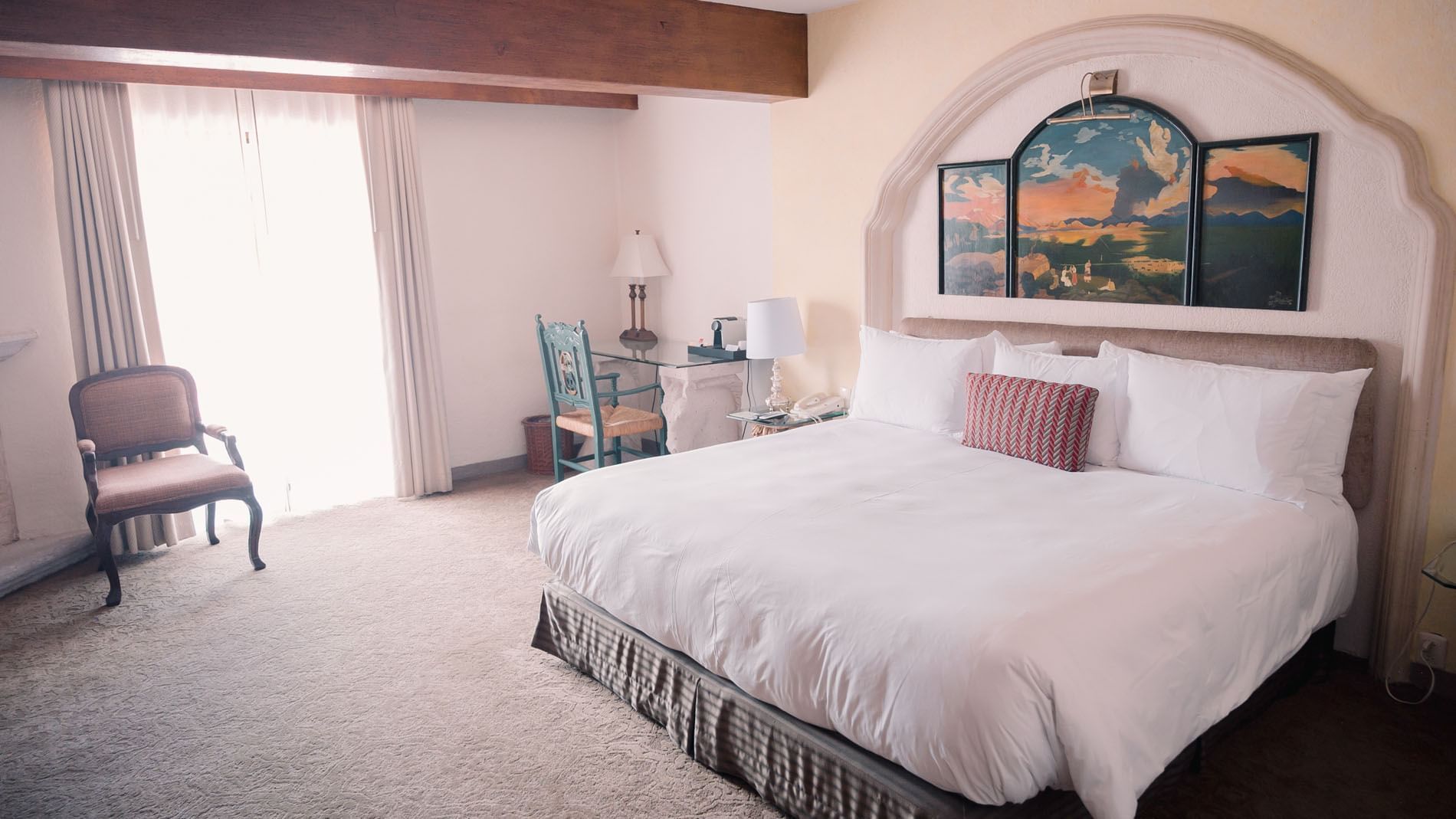 King Master Suite with white bedding, artwork, glass desk, chair, and window with curtains at Quinta Real Zacatecas