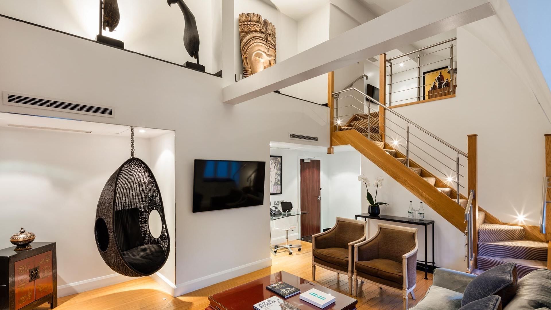 Modern living room with a floating staircase and hanging wicker chair in the Duplex Suite at The May Fair Hotel London