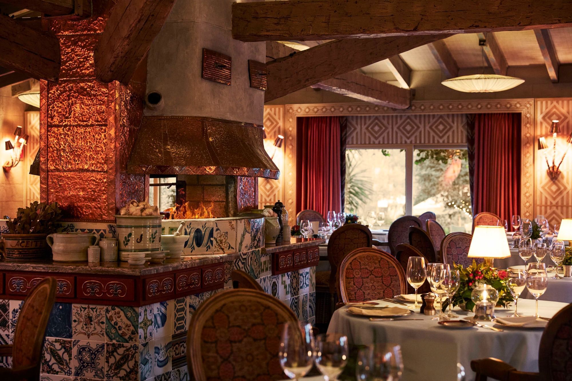 Elegant Marbella Club restaurant interior with a grand tiled fireplace, warm lighting, and beautifully set tables
