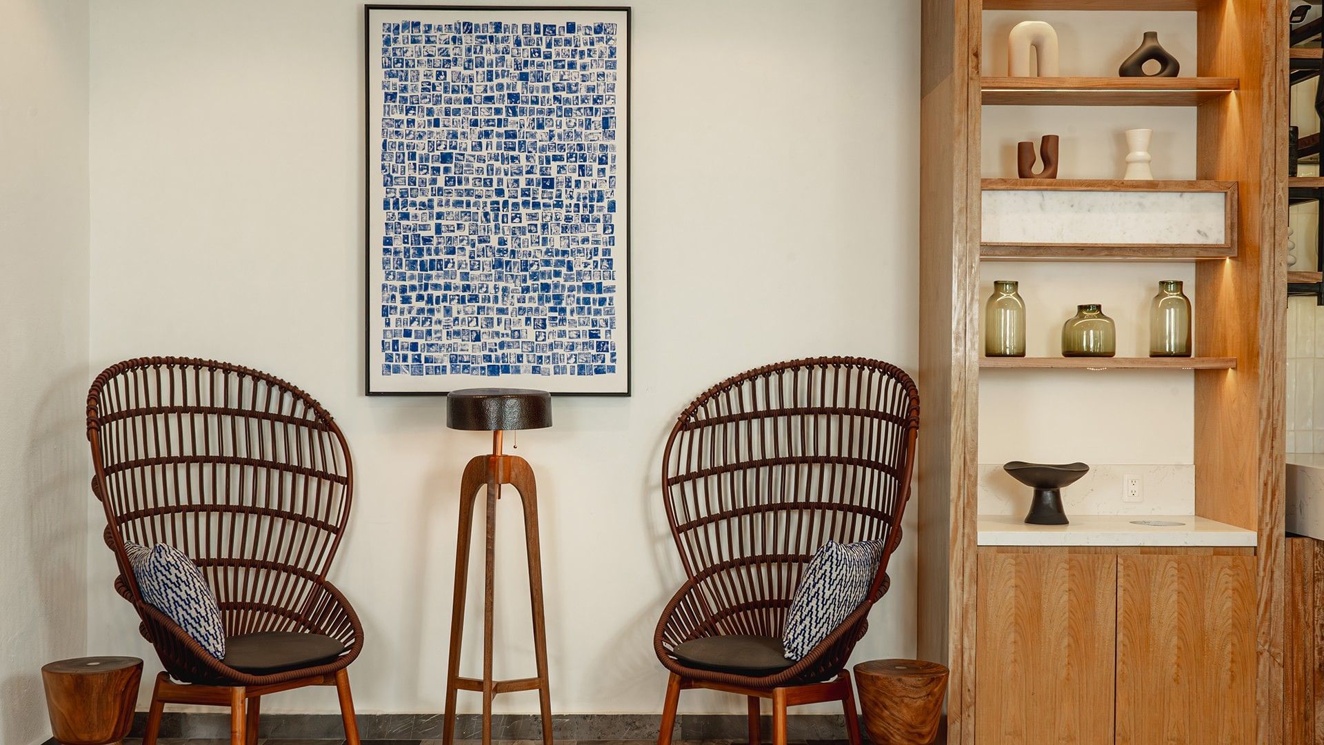 Abstract blue artwork and wooden shelves by two wicker chairs in Library Café & Deli at Camino Real Zaashila Huatulco