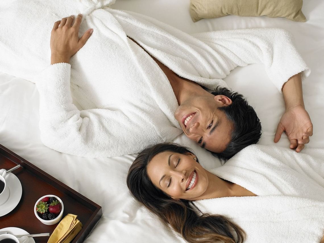 A couple in bathrobes & lying on the bed at Ana Hotels