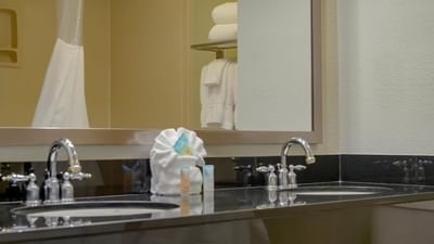 Dual sinks with chrome faucets by rolled towels on a granite vanity in King room at Galleria Palms Hotel