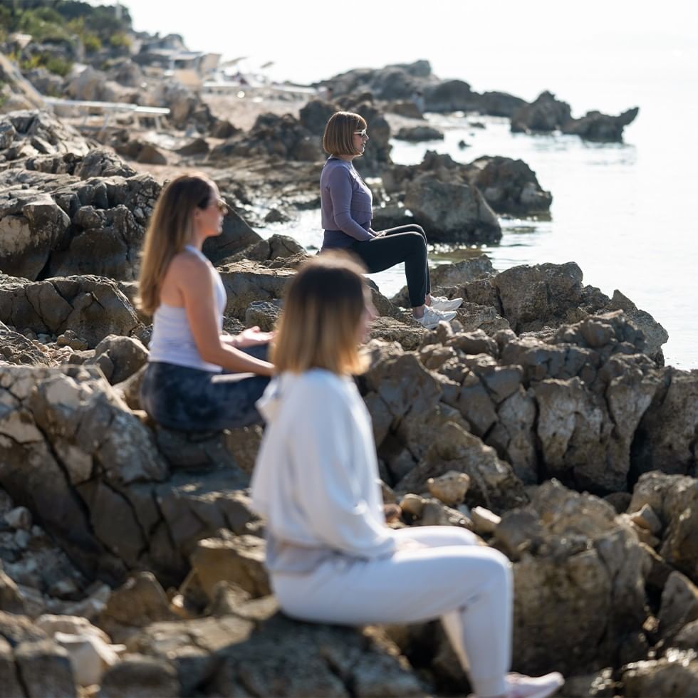 Drei Frauen praktizieren Sound & Inner Balance Retreat auf Felsen am Meer
