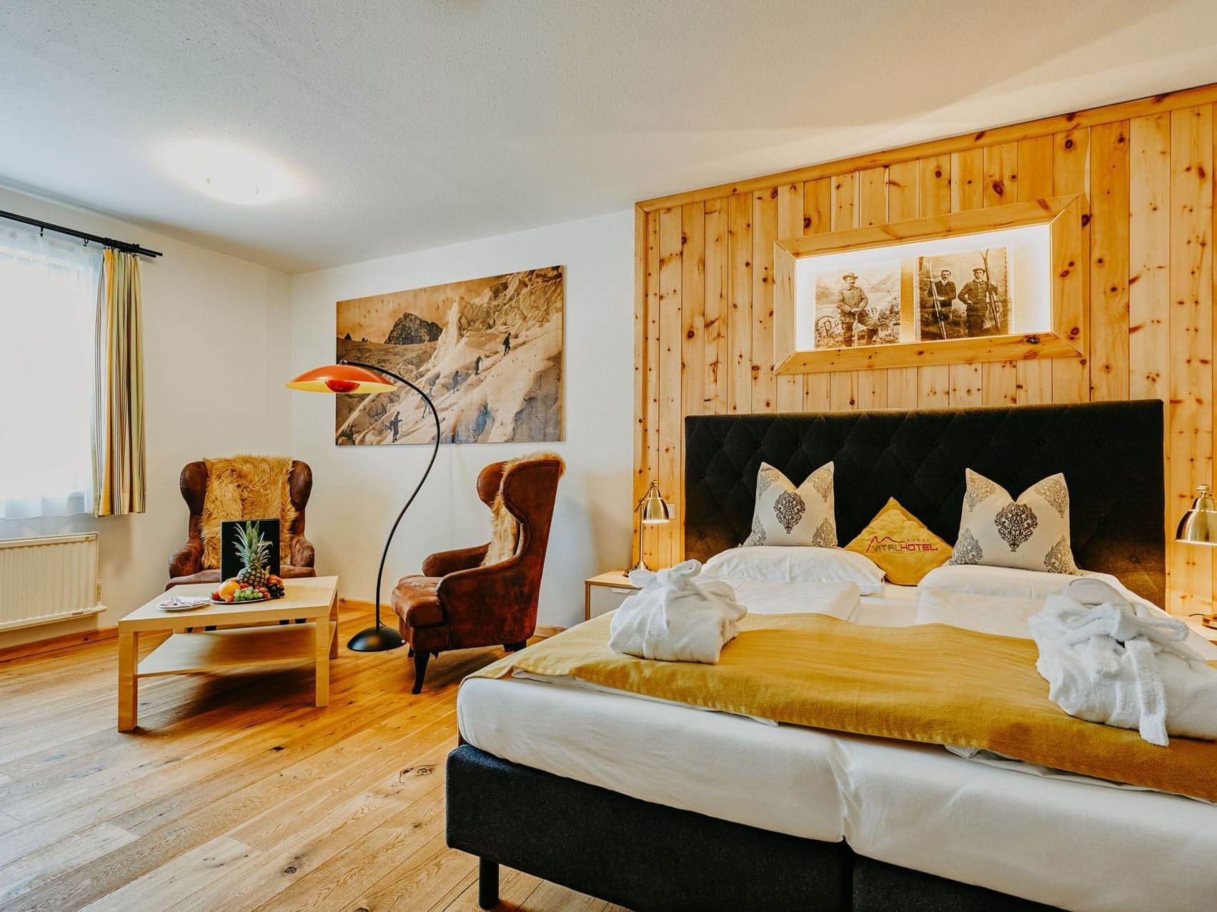 Gemütliches Hotelzimmer mit Holzwänden, großem Bett, Sesseln und einem Tisch.