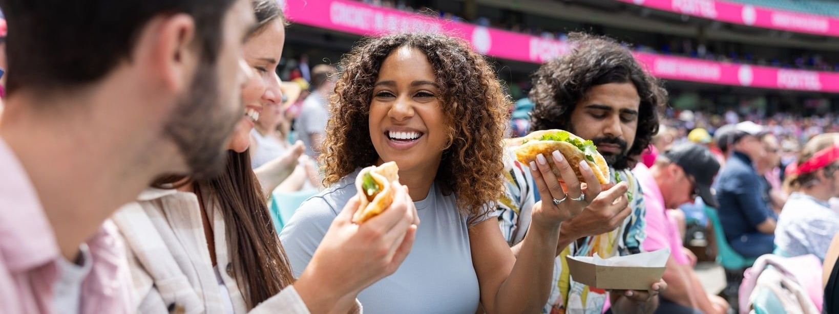 Friends enjoying burgers and drinks in stadium seating during the Australia v New Zealand Test Series 2027