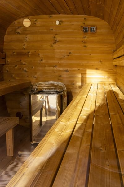Cozy indoor wooden barrel sauna interior with benches and a central electric heater stove at Rodd Moncton