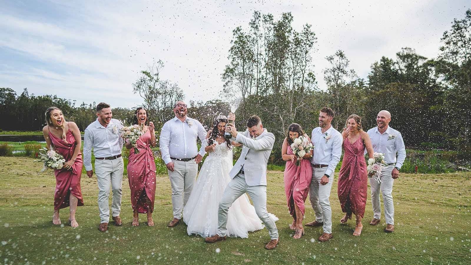A wedding party popping champagne outdoors with confetti in the air at Mercure Kooindah Waters