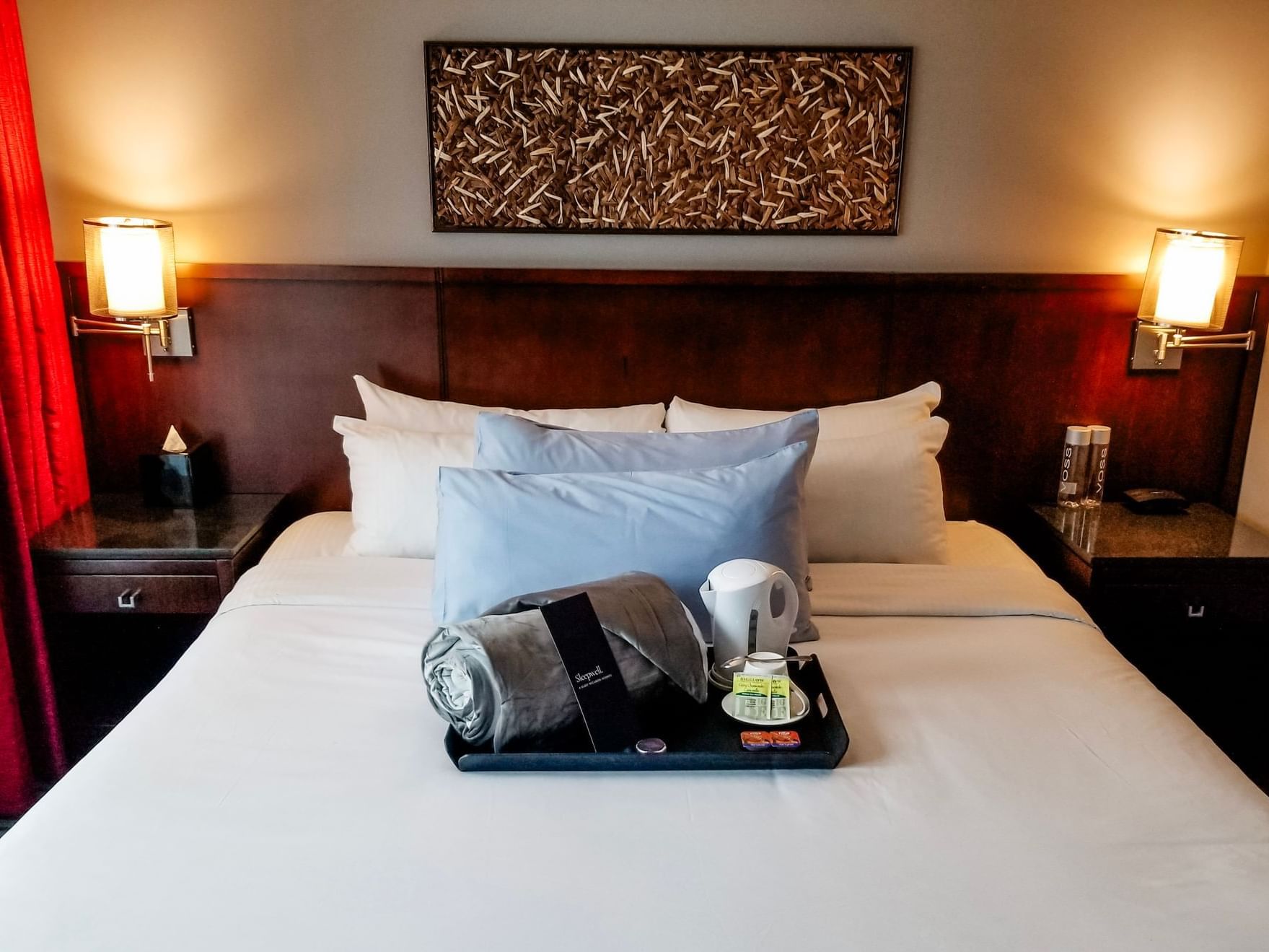 A neatly made bed with pillows, a cozy blanket, kettle, tea, and snacks on a tray at Matrix Hotel