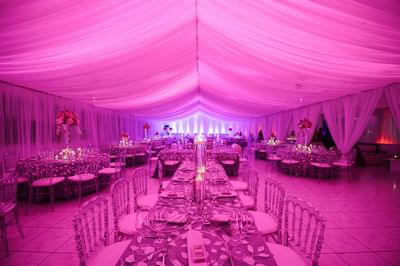 Long banquet table under a pink-lit draped tent, surrounded by clear chairs in Frank Room & Terrace at Hotel Montana Haiti