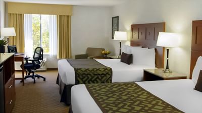Modern 2 Queen Room at Moab Valley Inn with two double beds, a desk, a comfy chair, and a large window with garden view