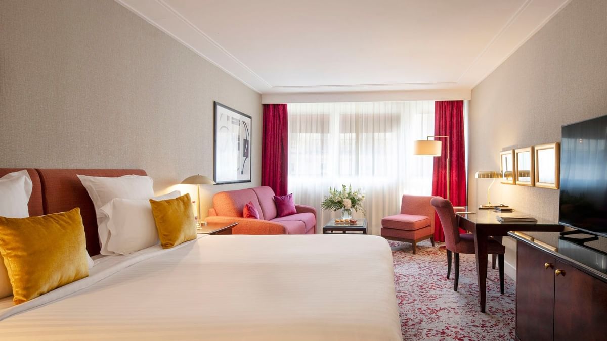 Plush bed by a pink sofa and armchair under soft lighting in Executive Room at Warwick Paris Champs Elysées