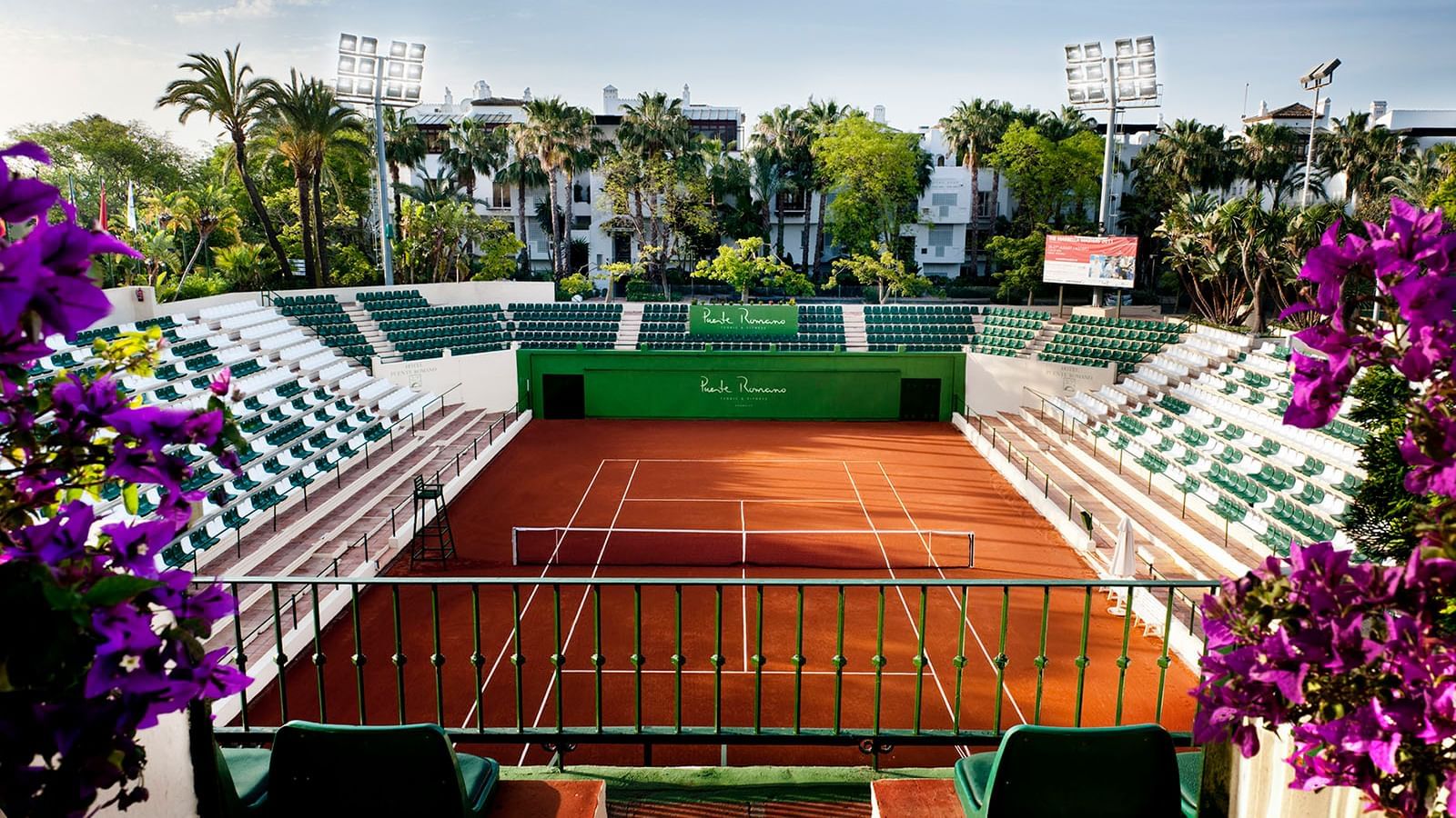 Overhead view of a Puente Romano Tennis Club, with palm trees and stadium seating near lighting at the Marbella Club
