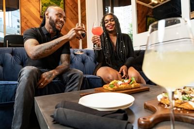 Guests raising wine glasses on a blue sofa by flatbread and tableware in the stylish lounge area at Hotel Saint Clair