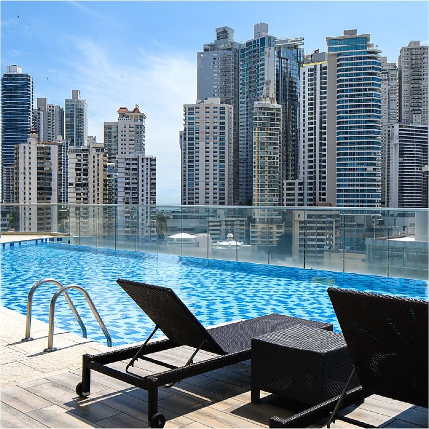 Dos tumbonas negras y una mesa junto a la barandilla de la piscina, ante vistas urbanas, en Megapolis Hotel Panama