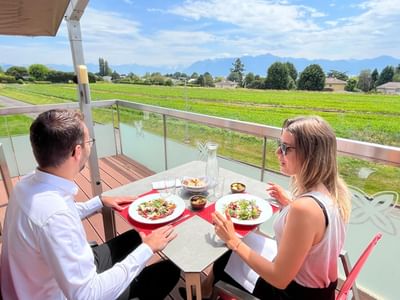 Couple enjoying a meal on a terrace with a view of a green field at Starling Hotel Lausanne