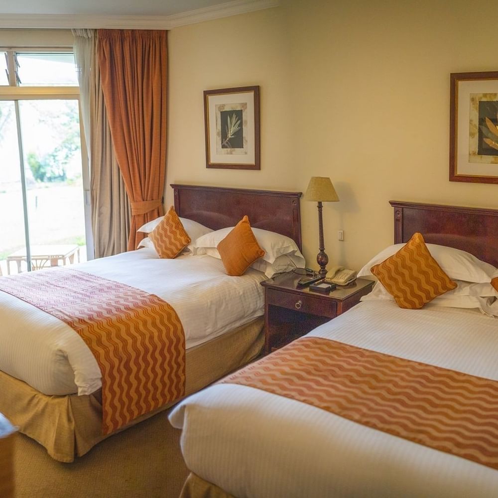 Two beds with orange and white linens in a family room at Lake Kivu Serena Hotel in Gisenyi.