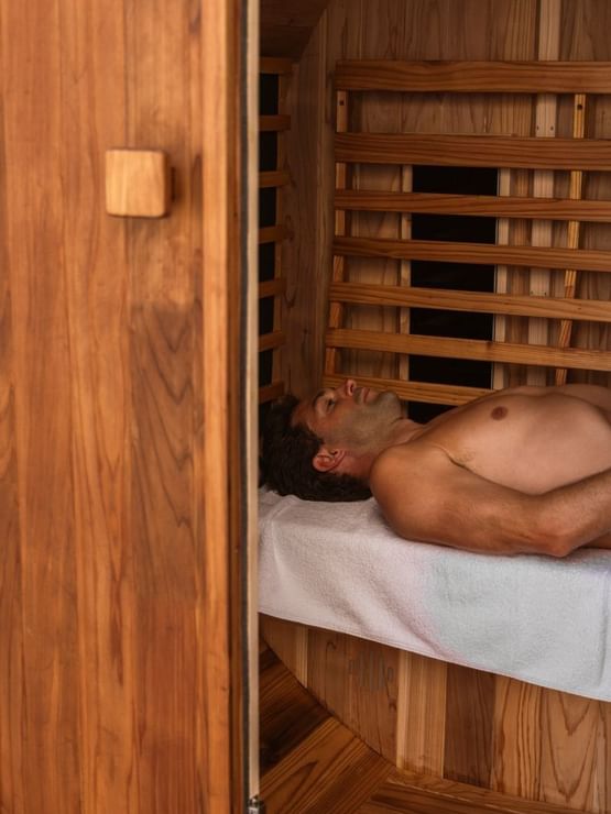 Man at Elysium Manly lying relaxed on a white towel with the wooden slats of the sauna wall, a featured hotel in Manly