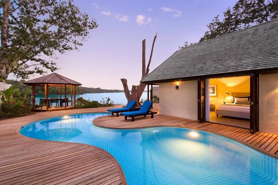 Efate Pool Villa featuring curved infinity pool and wooden deck with blue loungers at twilight at warwick le lagon-vanuatu 