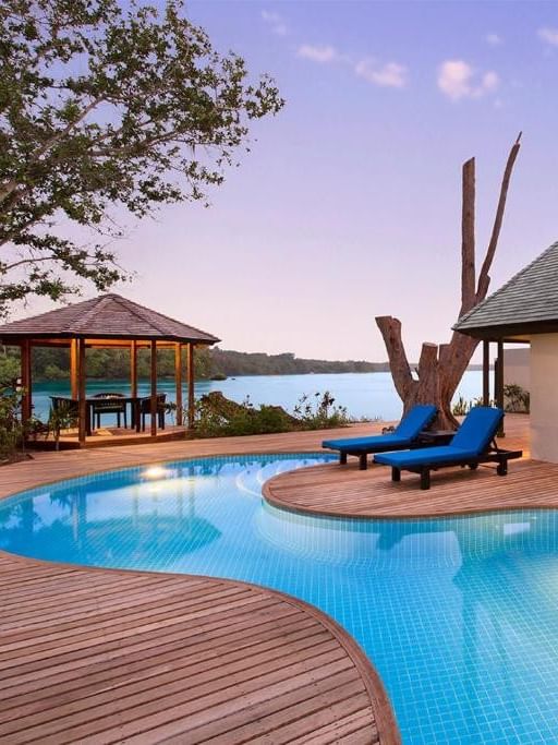 Efate Pool Villa featuring curved infinity pool and wooden deck with blue loungers at twilight at warwick le lagon-vanuatu 