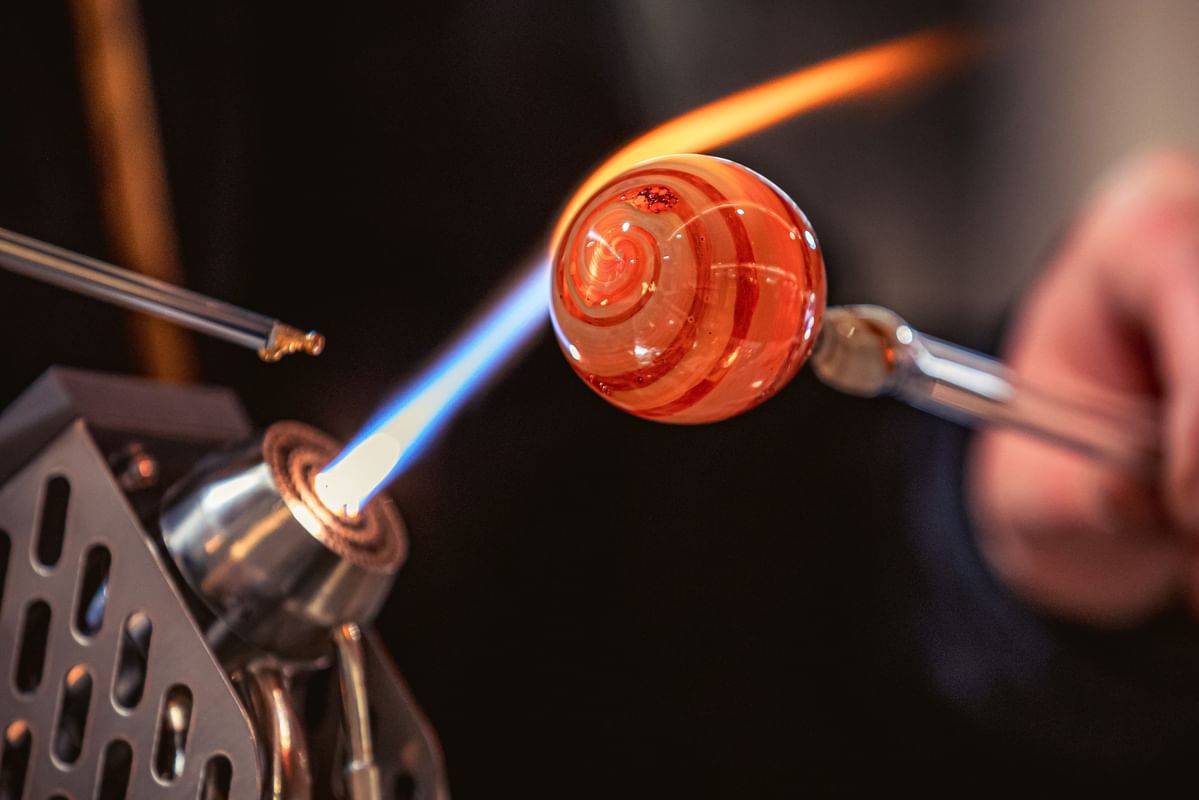 Molten glass orb with a red swirl shaped by a torch flame on a rod at Warwick Seattle