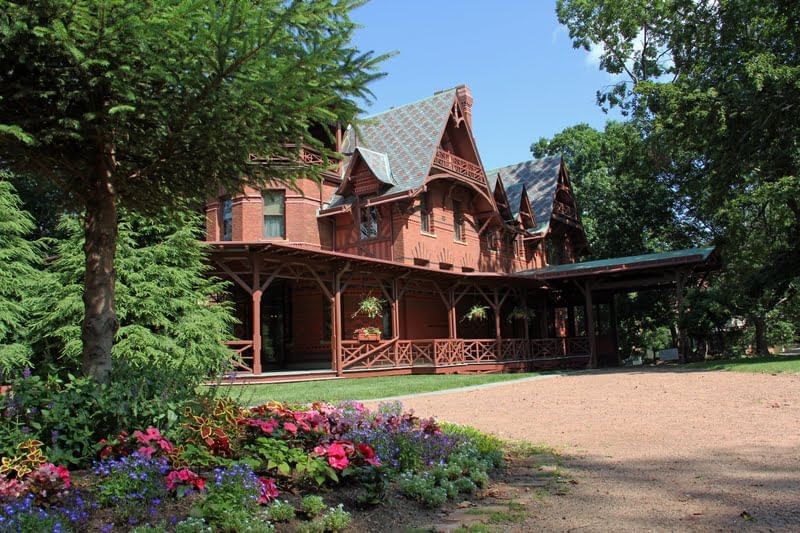 Exterior view of Mark Twain House with a large wooden porch and flower garden near Avon Old Farms Hotel