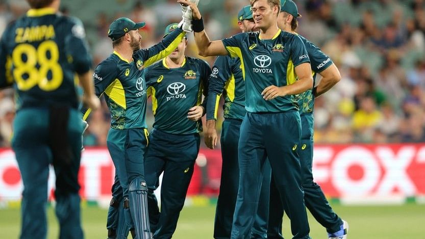 Cricket players in green and yellow uniforms celebrate on a field with a crowd in the background.