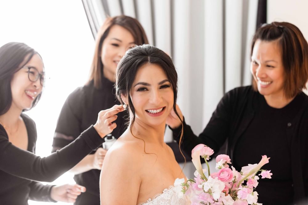 Joyful bride surrounded by her bridesmaids while preparing at El Prado Hotel