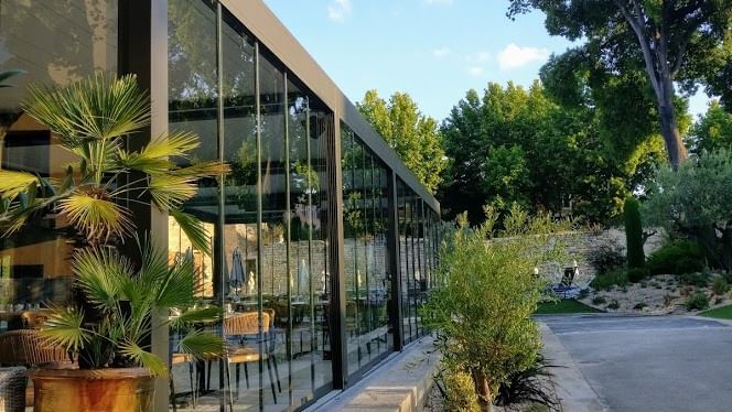 Façade moderne avec verre et plantes, bordée d'une route et d'arbres sous un ciel bleu.