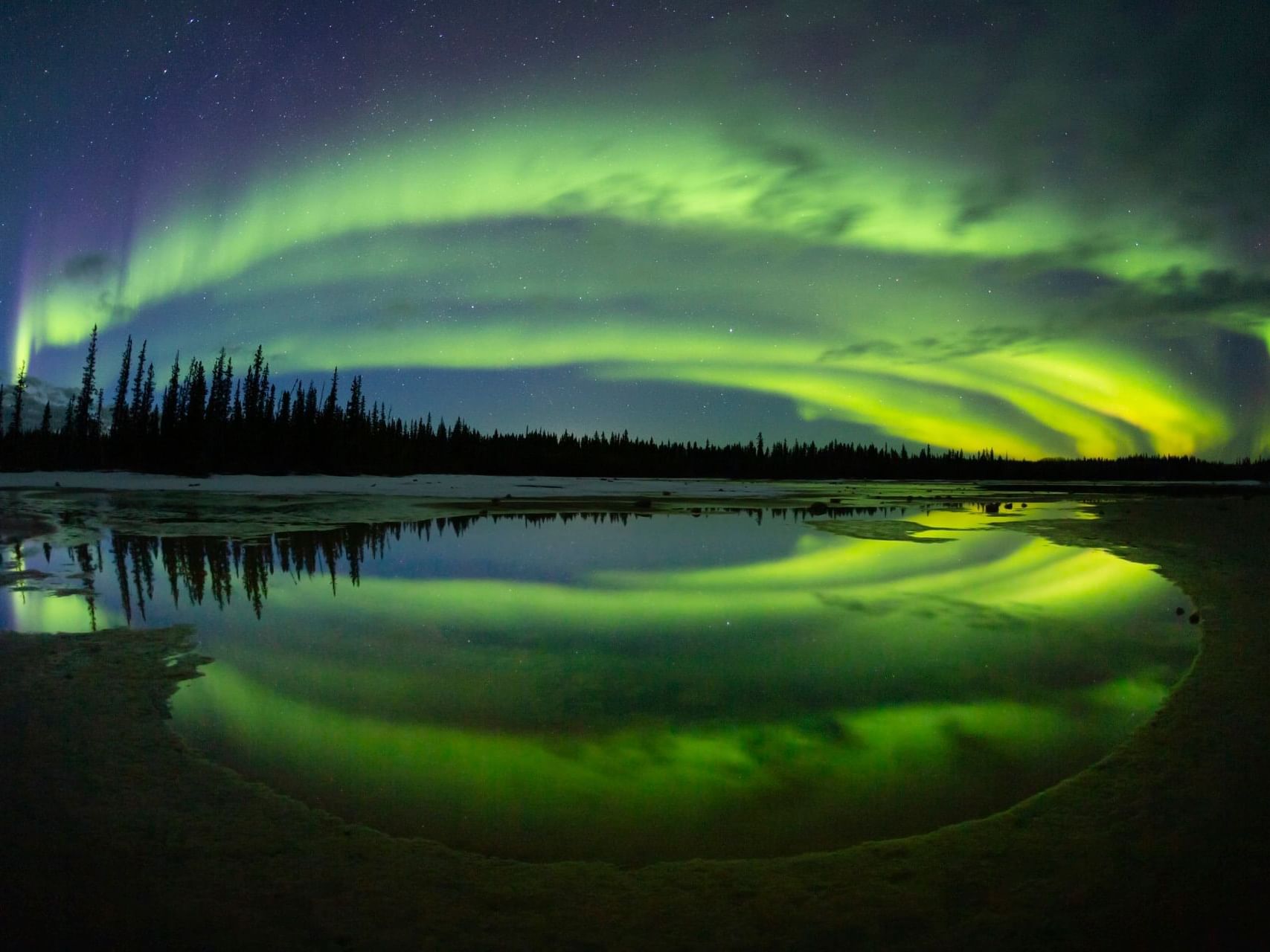 Northern Lights in the sky over a lake near Merit Hotel & Suites