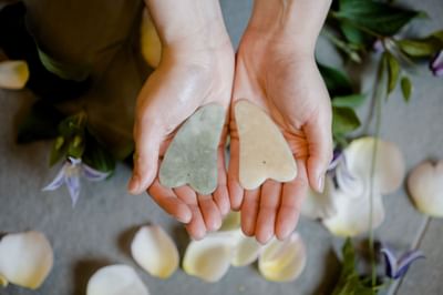 Pair of hands holding two smooth gua sha massage stones above flower petals on floor at La Tourelle Hotel and Spa