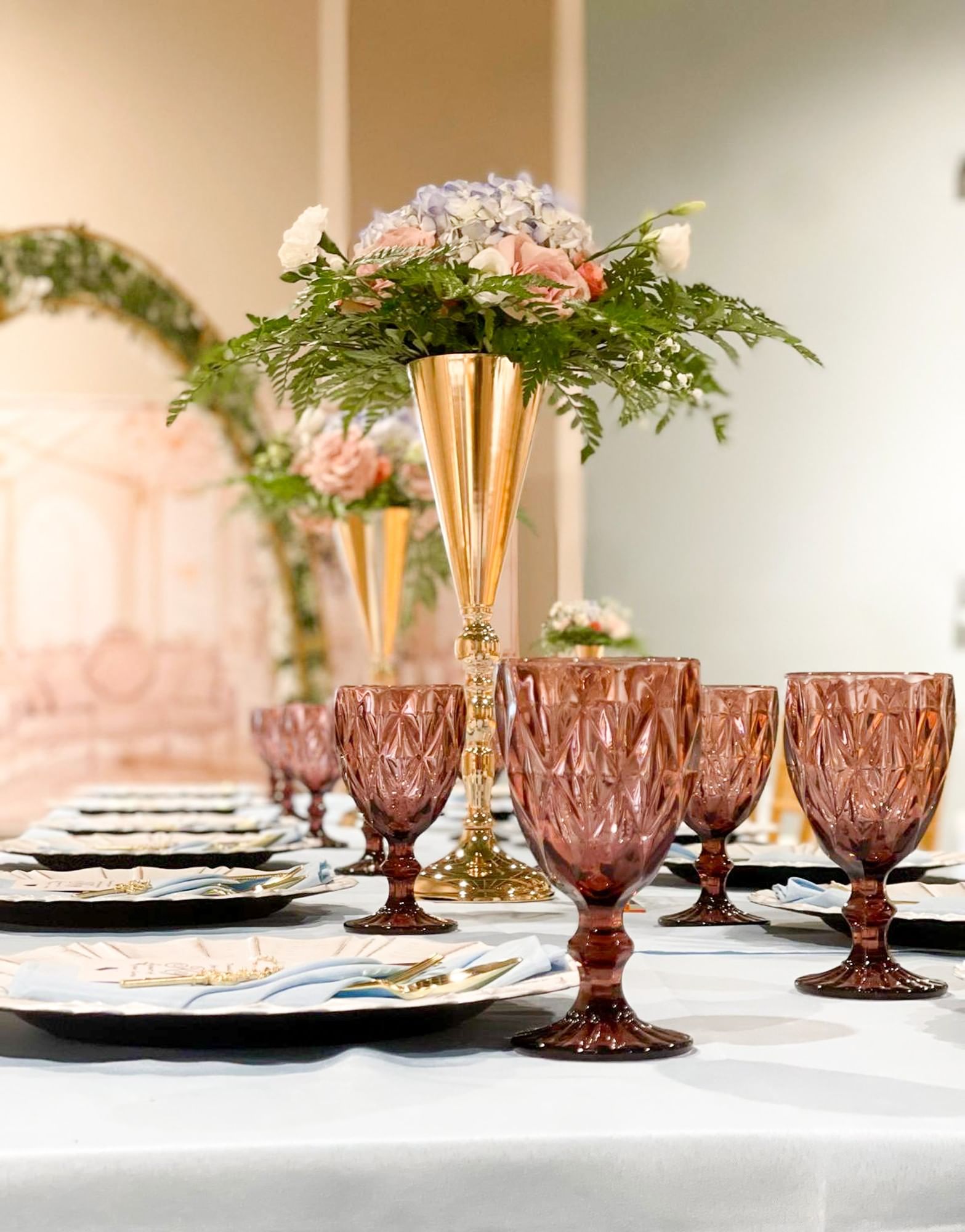 a dining table set with glasses, plates, and flowers