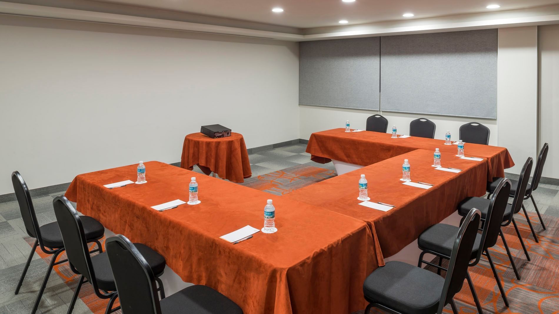 U-shaped Kyoto conference setup with orange table linens, black chairs, and bottled water at Real Inn Celaya