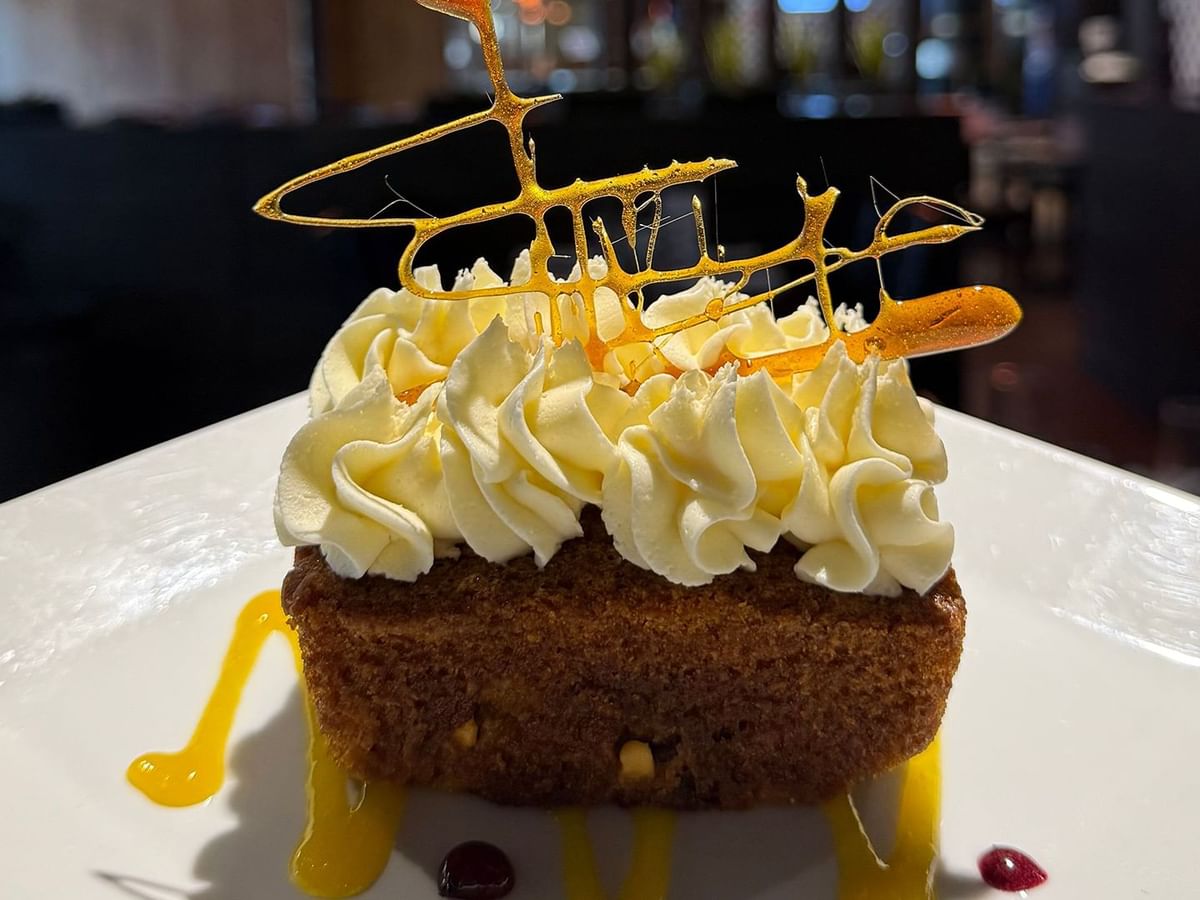 A slice of toffee cake with whipped cream and caramel sauce on a white plate in a restaurant.
