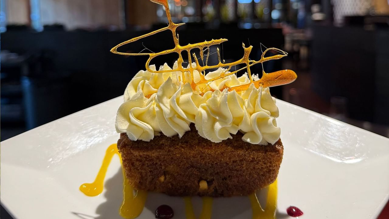 A slice of toffee cake with whipped cream and caramel sauce on a white plate in a restaurant.