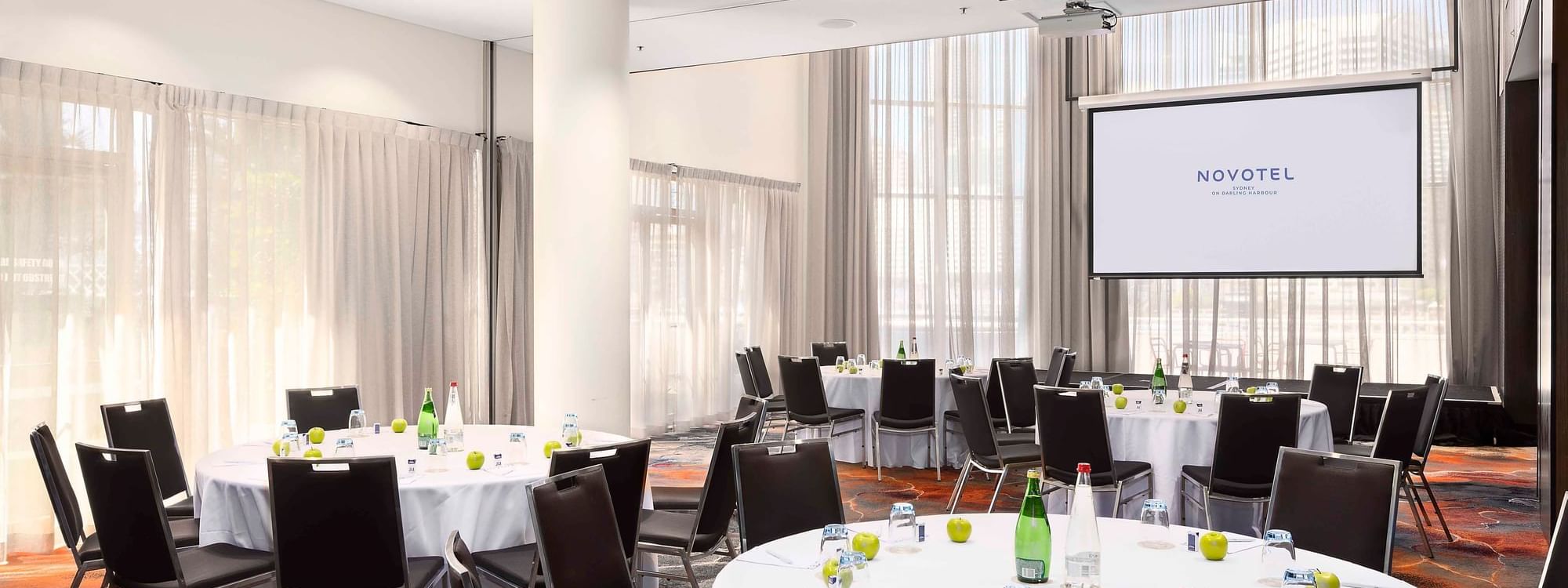 Banquets set up facing the projector screen in The Hunter Room 1-3 at Novotel Sydney on Darling Harbour