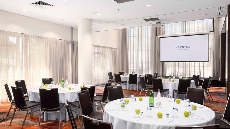 Banquets set up facing the projector screen in The Hunter Room 1-3 at Novotel Sydney on Darling Harbour