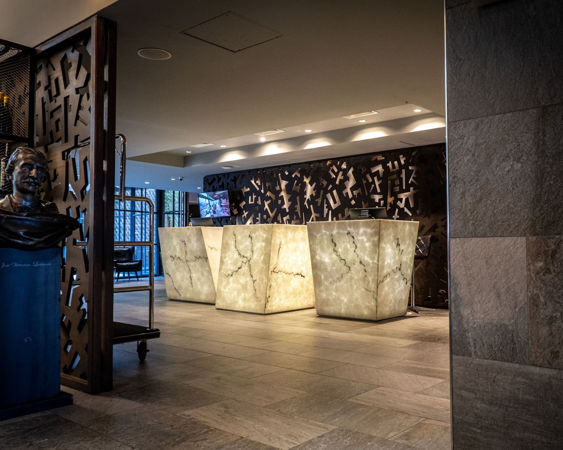 Recepción moderna con mostrador de mármol iluminado y arte decorativo en Cumbres Lastarria