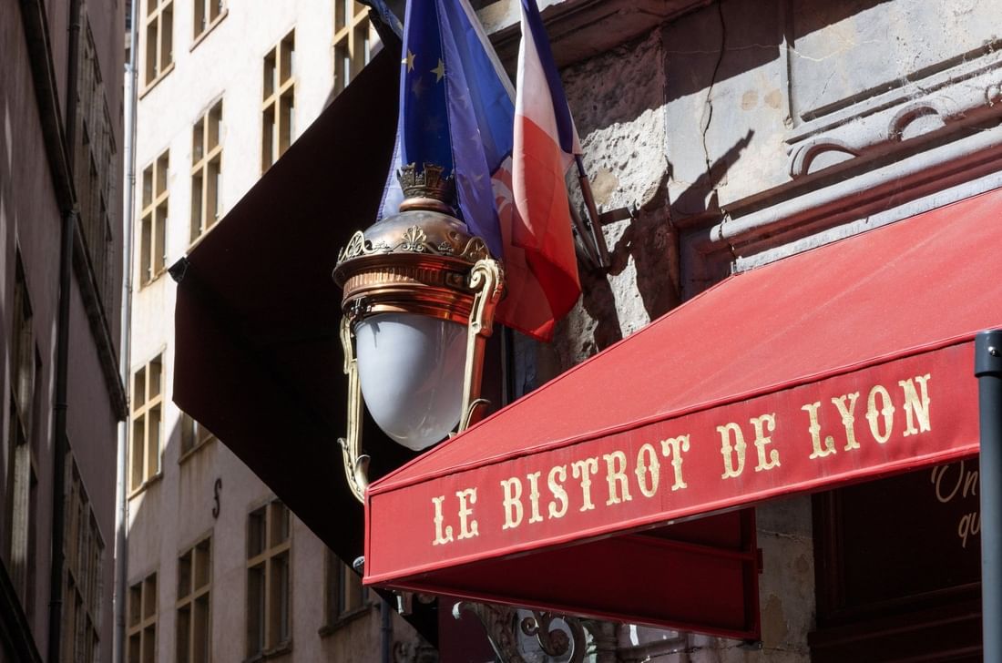 Enseigne rouge d'un bistrot lyonnais avec drapeaux français et européen et lampadaire décoratif au Warwick Reine Astrid-Lyon