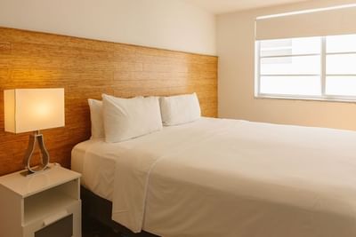 Bed by a nightstand under a polished wood panel headboard in Standard King Room at Aqua Hotel and Suites