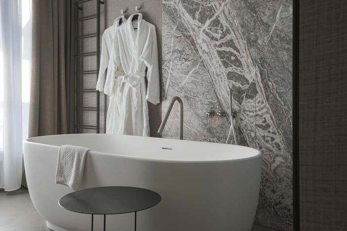 Bagno elegante con vasca bianca, asciugamani, e marmo a parete da DUPARC Contemporary Suites