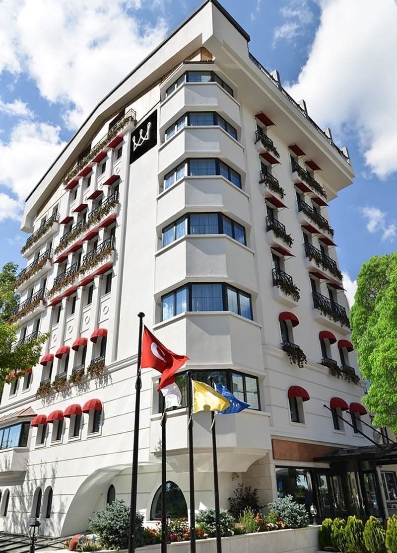 View of Warwick Ankara by green trees surrounding colorful flags under red window awnings