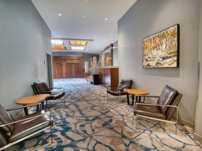 A hallway with leather chairs, circular tables, and a colorful painting at Matrix Hotel
