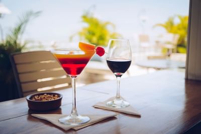Martini and red wine glasses by a bowl of nuts on a wooden table under palm trees at Hotel Montana Haiti