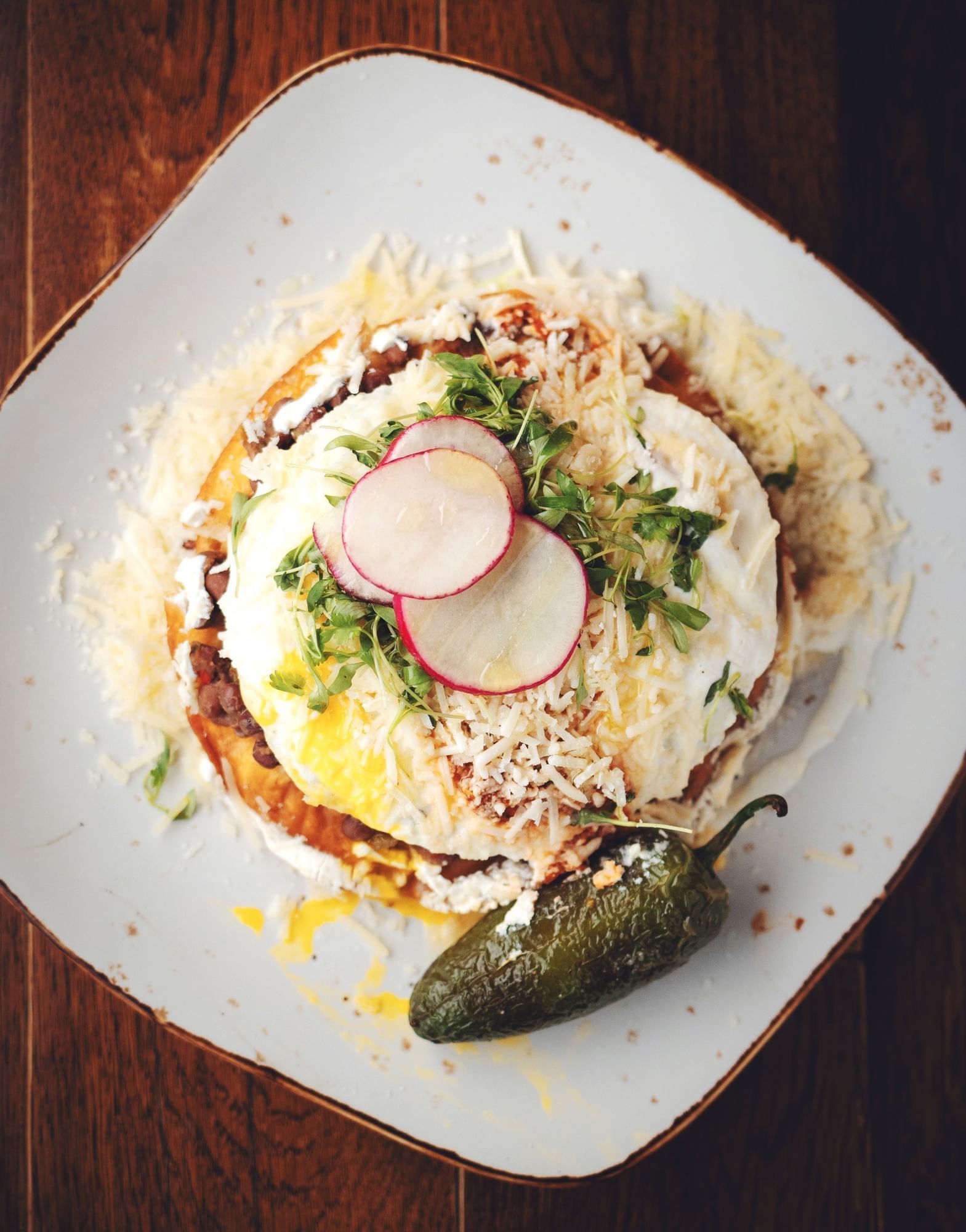 Lorem ipsum Overview shot of plate with eggs topped with cheese, cilantro, cheese, sliced radish and a grilled jalapeno on the side