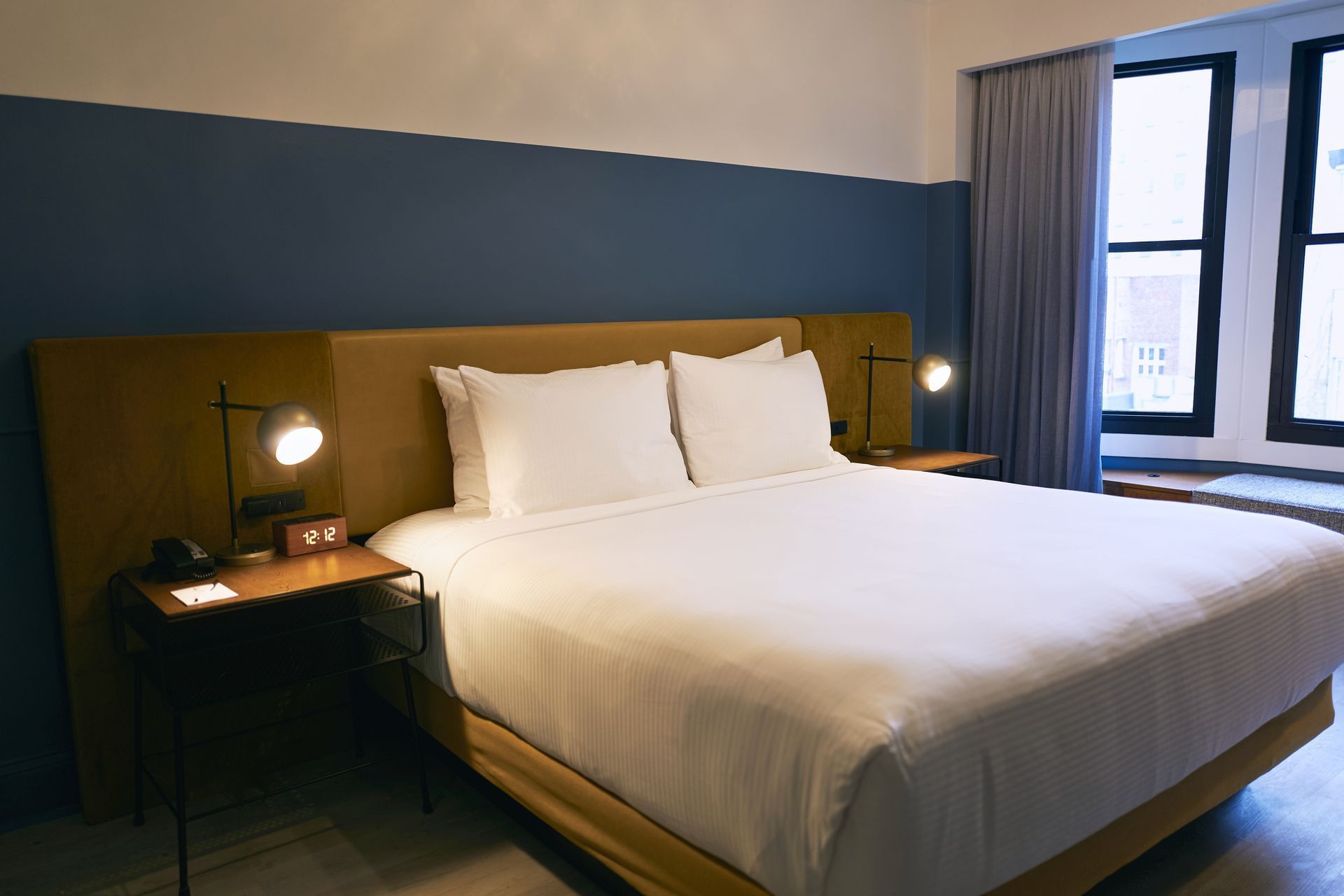 A hotel room with a king-sized bed, two nightstands with lamps, and a window with a curtain.