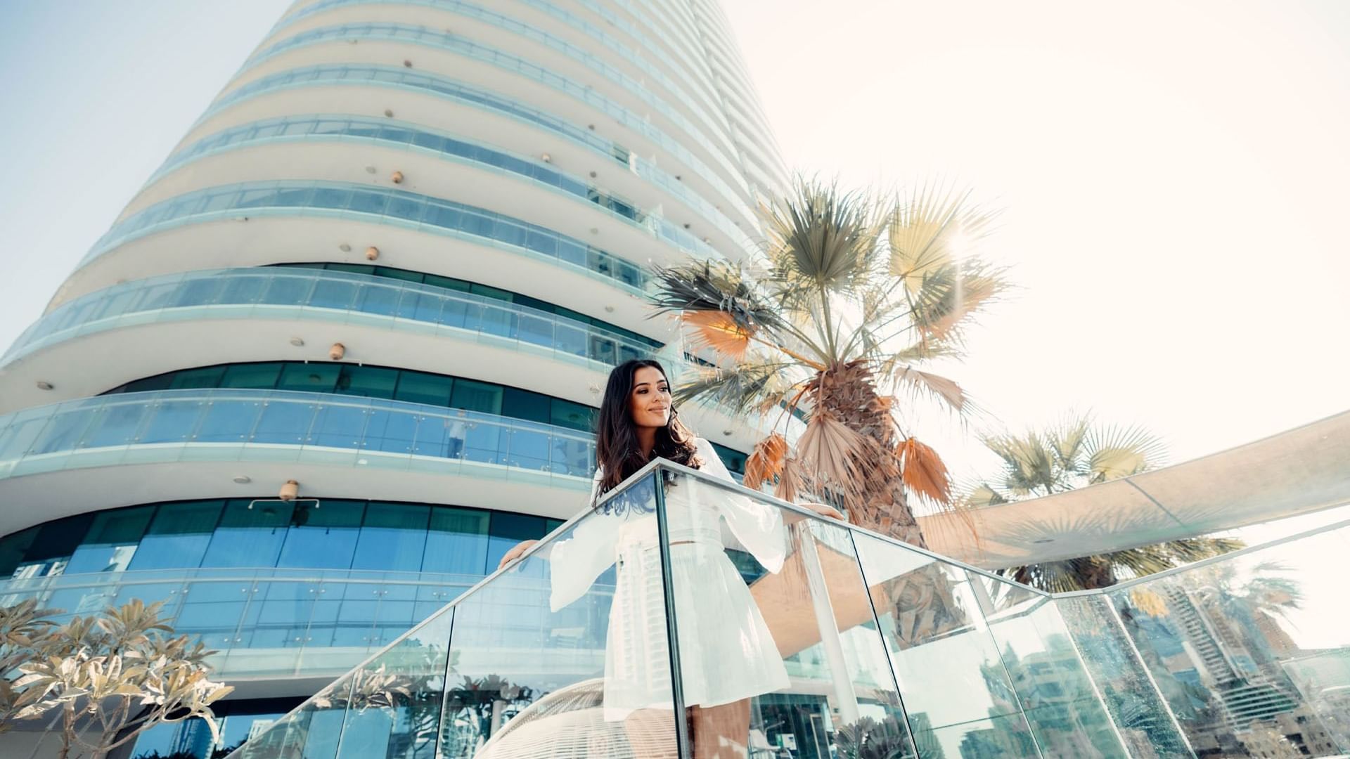 A woman in a white dress standing on a balcony overlooking the city at DAMAC Maison Distinction