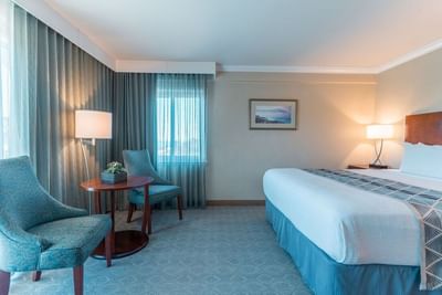 A bright and spacious room with a king bed, two teal accent chairs, and sheer curtains at Carmel Bay View Inn