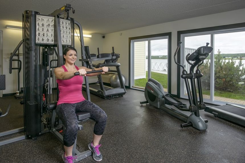 Guest exercising on a multi-gym machine by large sliding glass doors under bright lights at Rodd Miramichi River